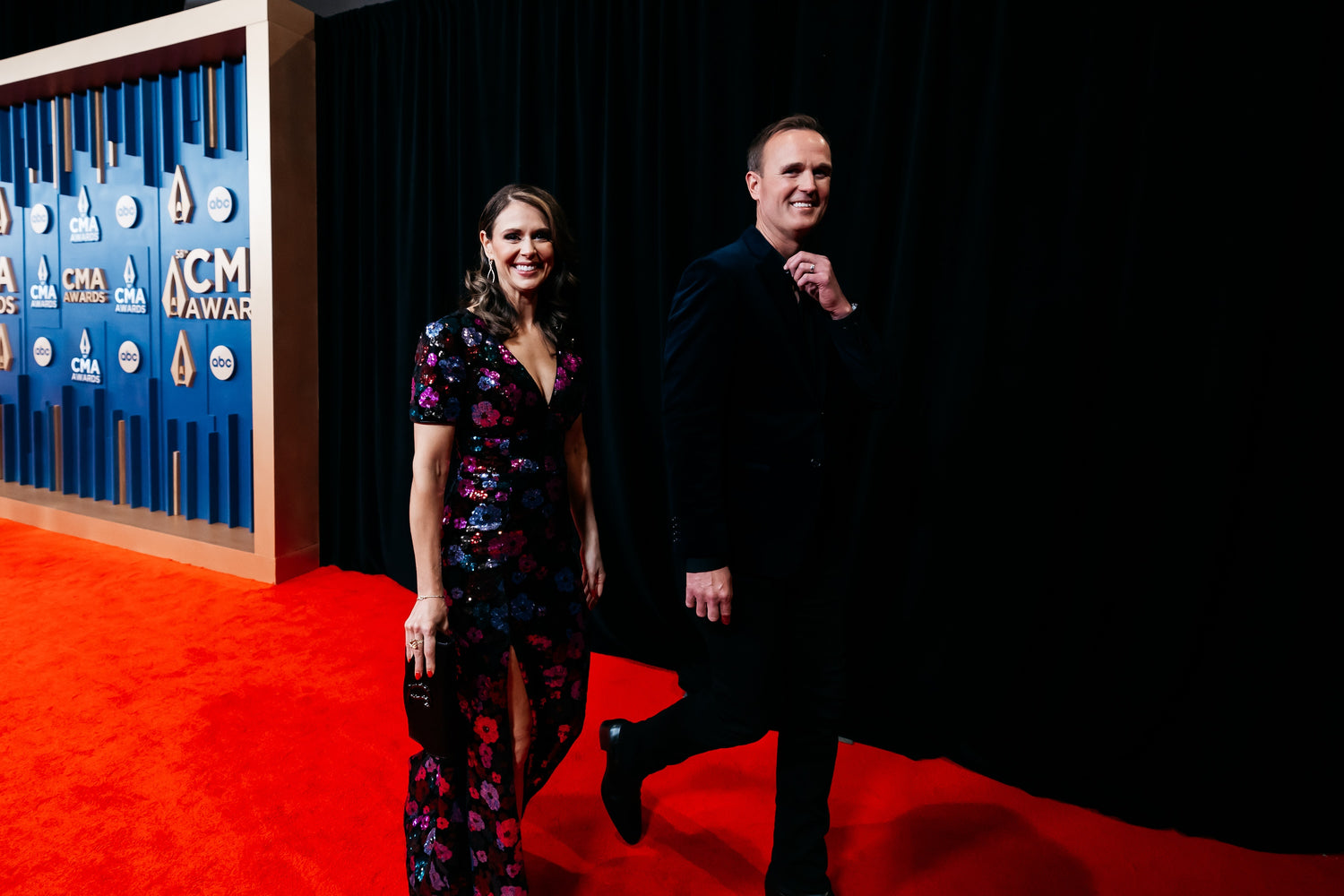 Two people standing on a red carpet with an ACM Awards backdrop