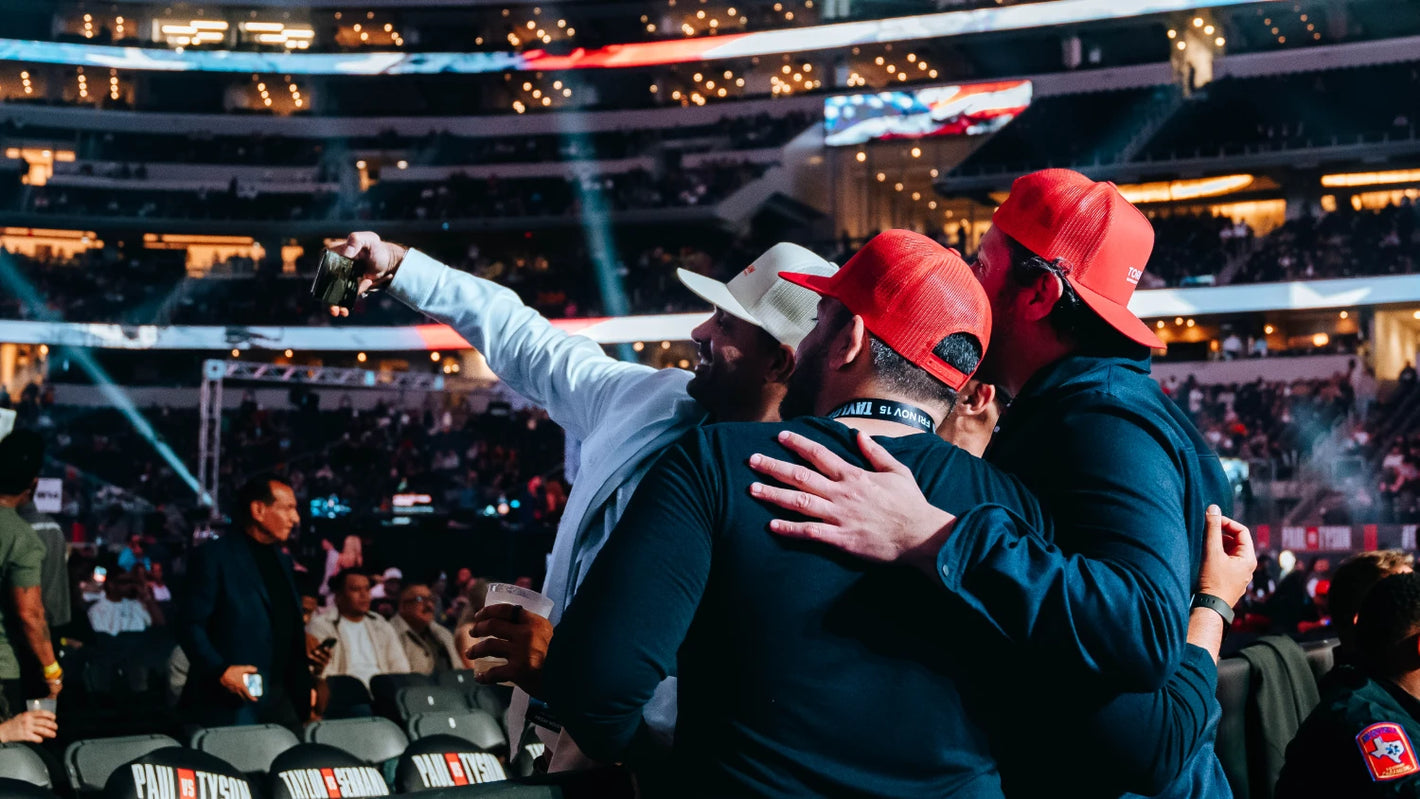 A group of three men take a selfie on a phone on the floor section of AT&T Stadium for an MVP Fight featuring Jake Paul. 